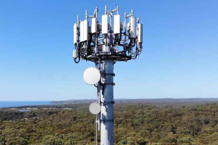 Large 5G cellular tower with multiple mmWave transceivers against a blue sky.