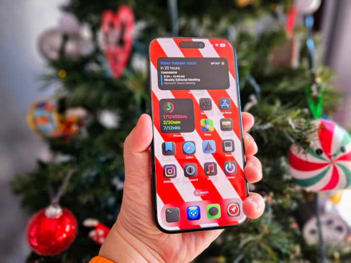 iPhone 15 Pro held in hand in front of a Christmas tree.